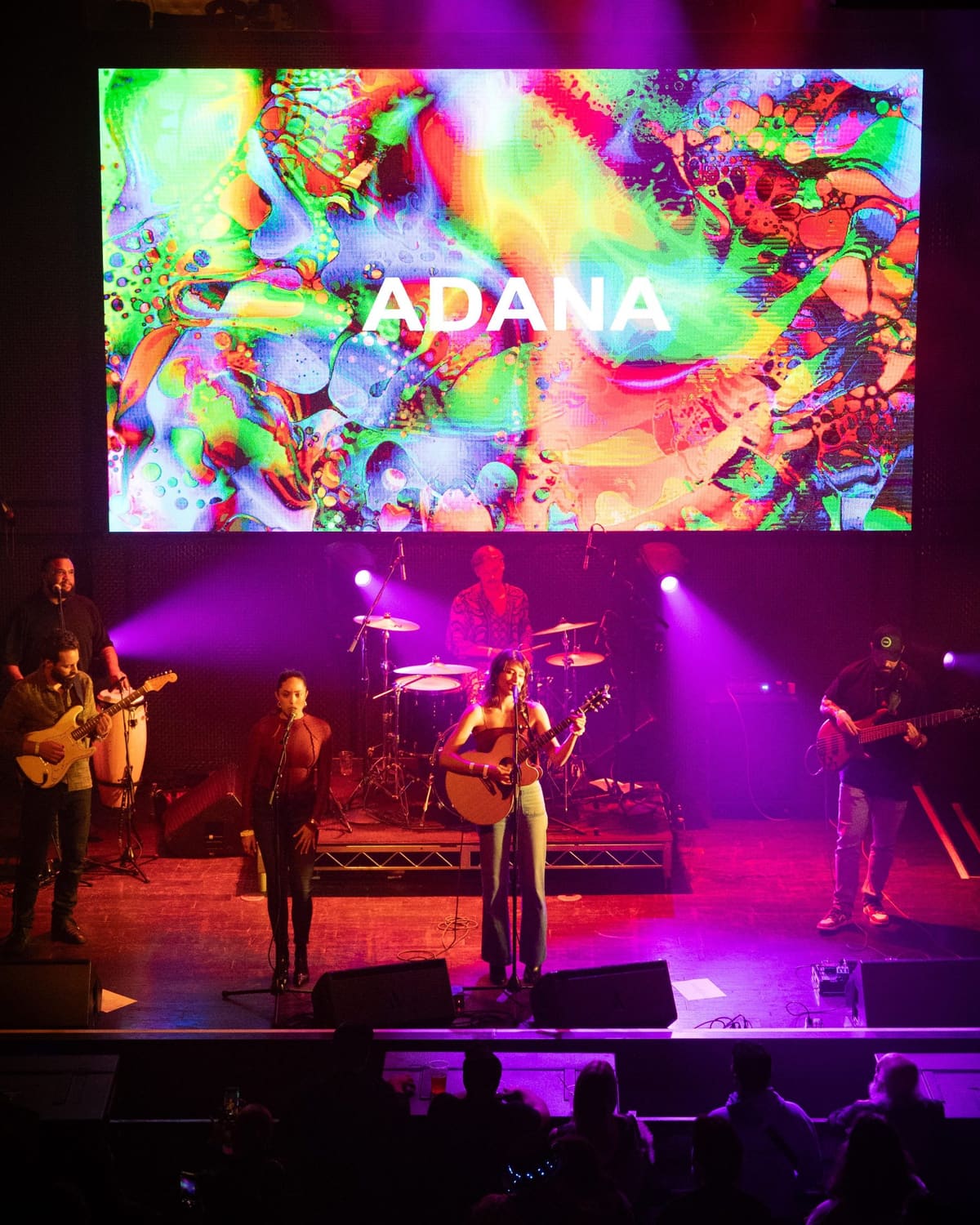 Adana performing live on stage under purple lighting